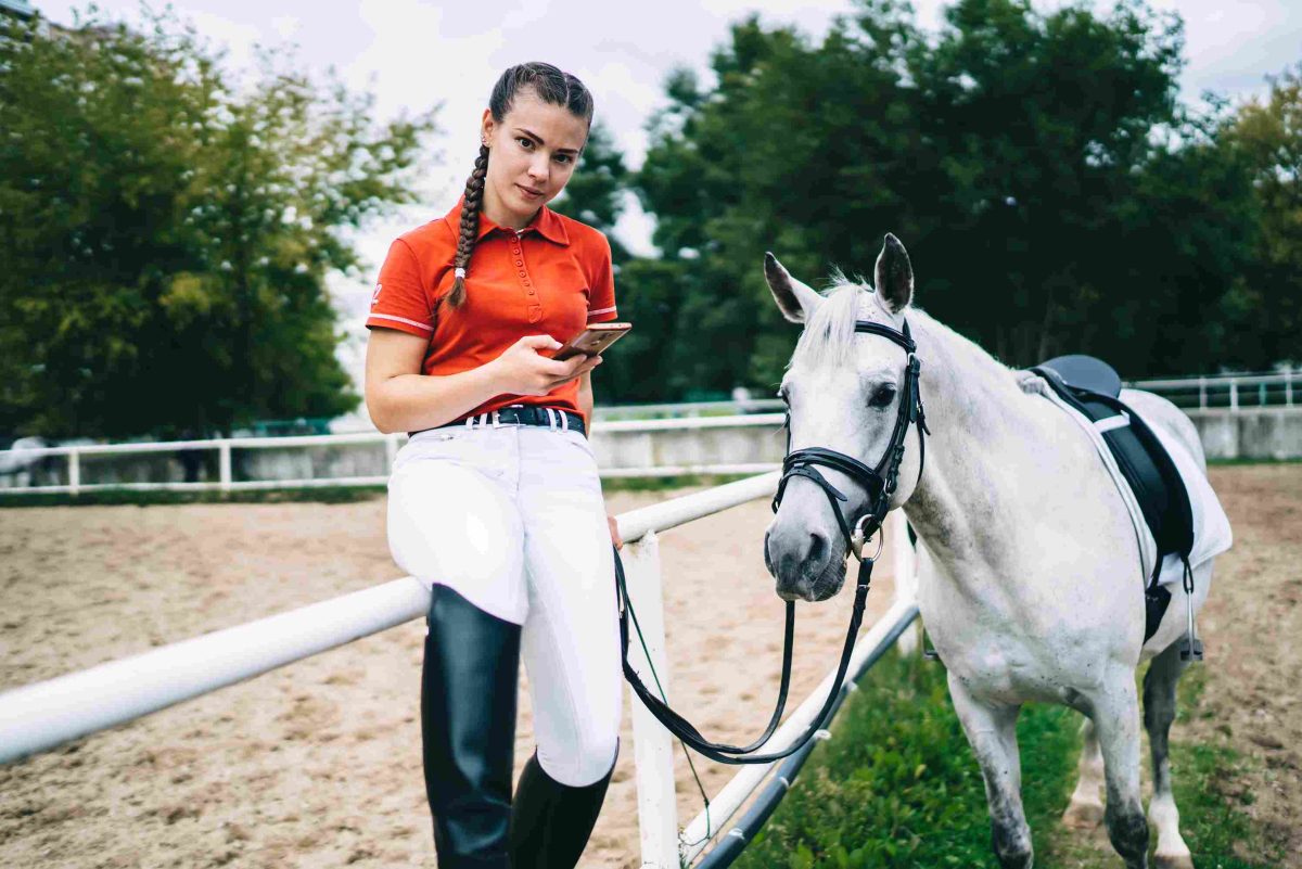 Portrait d’une cavalière après un entraînement de dressage avec un étalon, utilisant une application liée à horsetime sur smartphone pour gérer ses séances d’équitation et son planning équestre